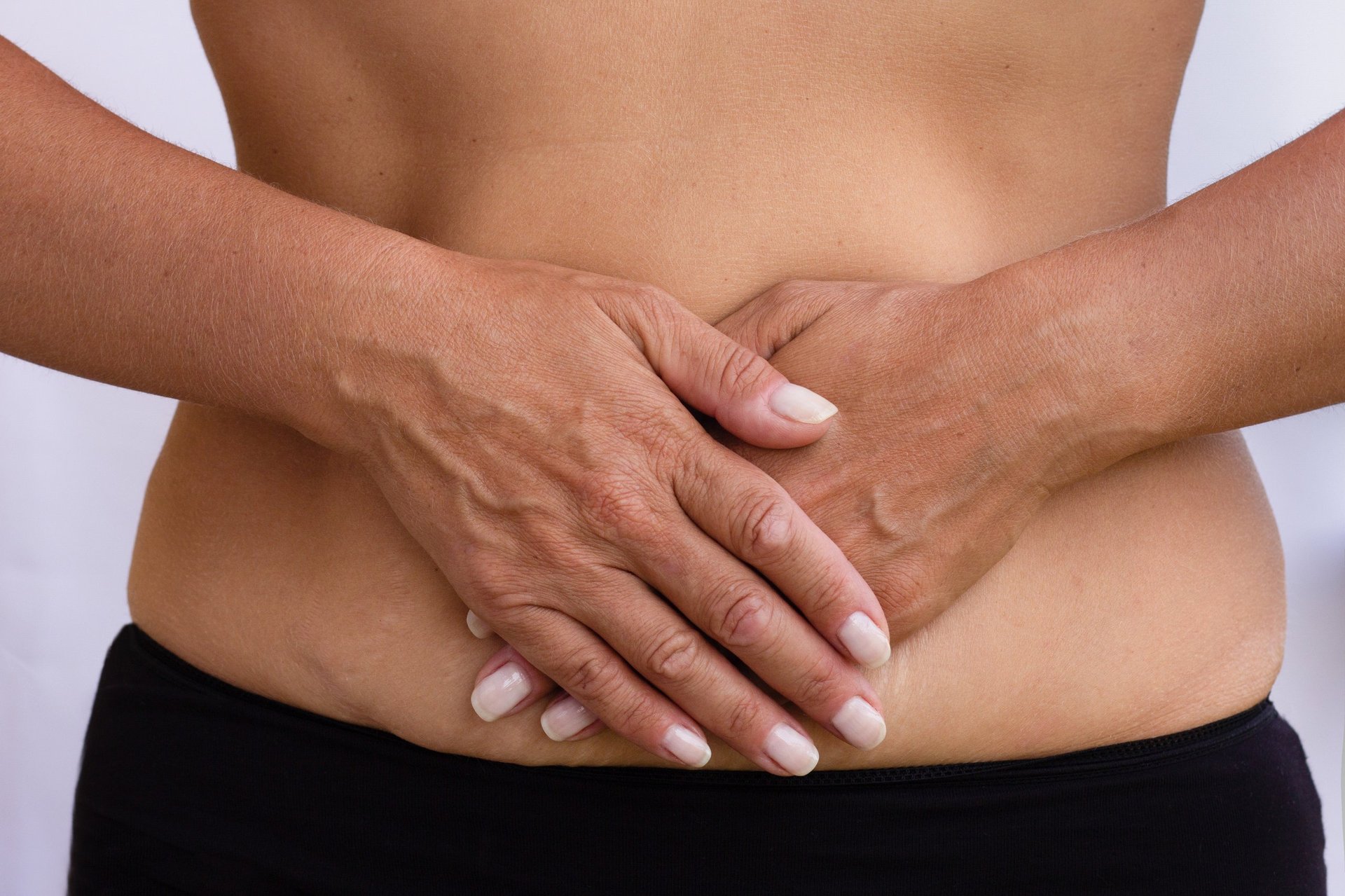 Woman's hands resting gently over her lower abdomen, reflecting body wellness and restoration