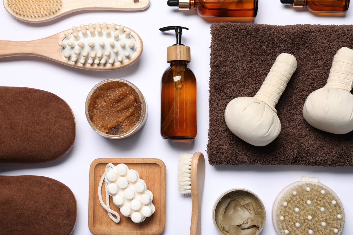 Flat lay composition with spa essentials including massage cream, wooden body contouring tools, essential oils, and soft white towels for holistic wellness training