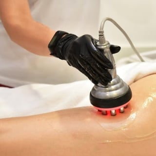 Person in black glove using handheld massage device with red nodules on someones arm during spa treatment